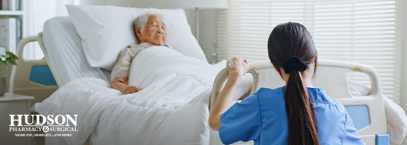 Senior man asleep in a hospital bed at an assisted living facility with a nurse adjusting the bed at the foot of the bed