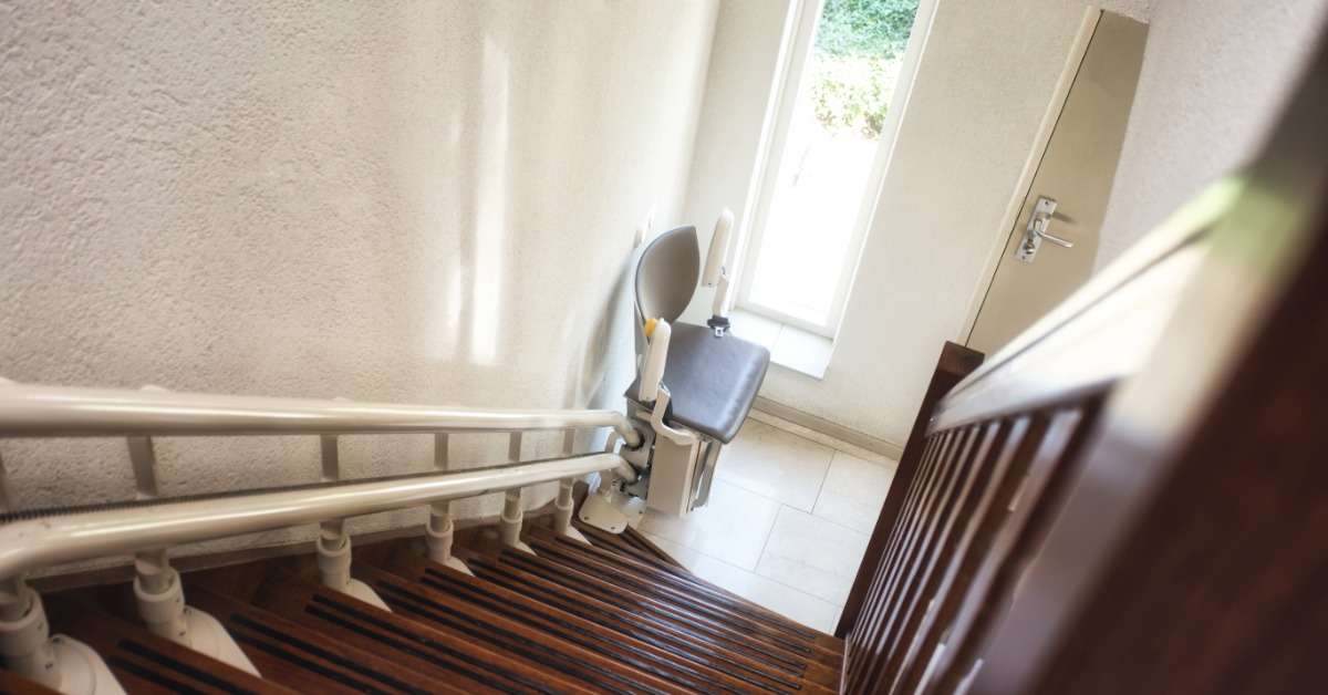 A view from the top of a residential staircase with a straight stairlift parked at the base of the steps.
