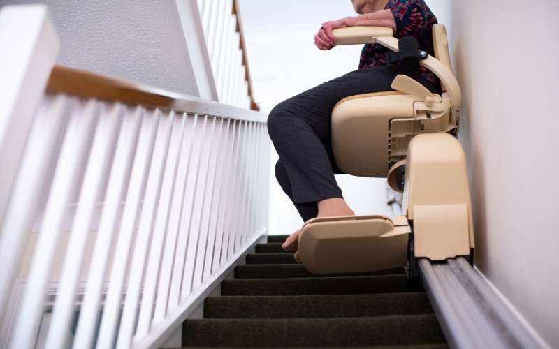 A close-up of a home stairwell with a stairlift user going up the stairs on the lift. The lift is secure to the wall.