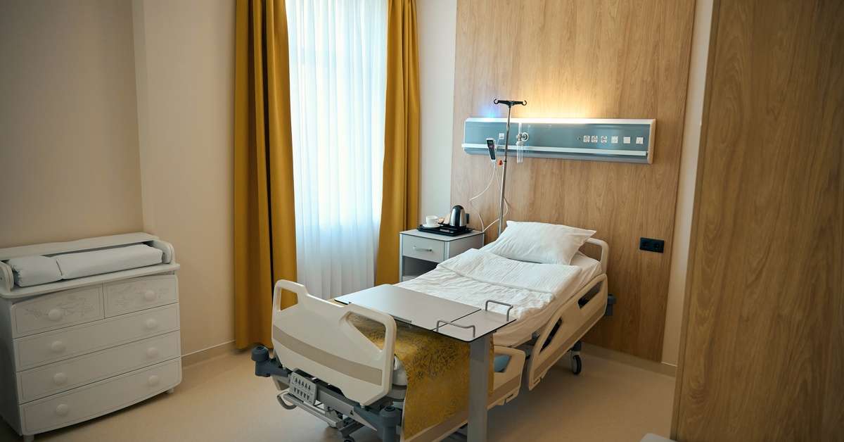 A rehabilitation center room with a hospital bed in the center. The tray rests over the bed, and the curtains are pulled.
