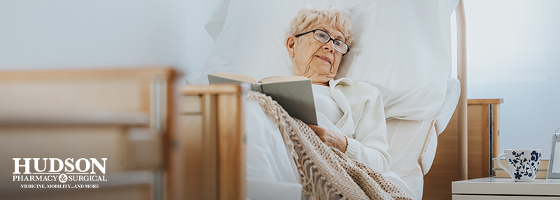Senior woman lying in hospital bed at home reading a book