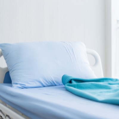 A close-up of a hospital bed rental in a facility. The bed has light blue linens and a teal blanket.
