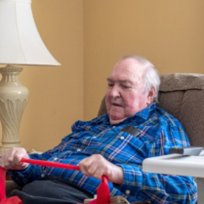 A senior man sits in his lift chair comfortably at home. He holds onto a red band for mobility exercises.