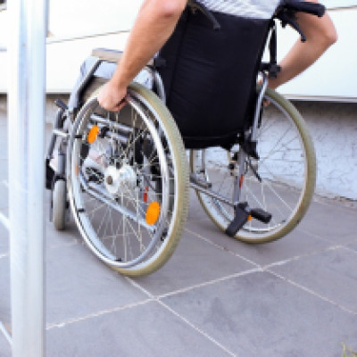 A person in a wheelchair rides their way up the ramp. The ramp is metal and the full-length of the sidewalk.