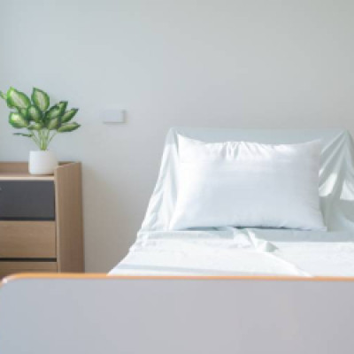 A home medical bed with white linens sits independently in a room. There is a nightstand to the left of the bed.