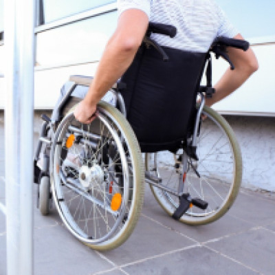 A wheelchair user using an exterior ADA wheelchair ramp. The ramp is steel with a low slope and a handrail.