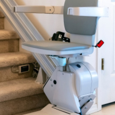 An electric motorized stairlift chair is sitting at the bottom of a carpeted residential staircase.