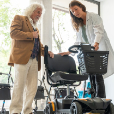 A senior man stands with a pharmacy professional as they discuss an electric scooter in the storefront.