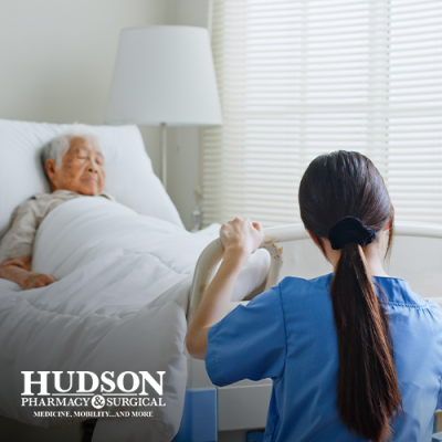 Senior man asleep in a hospital bed at an assisted living facility with a nurse adjusting the bed at the foot of the bed
