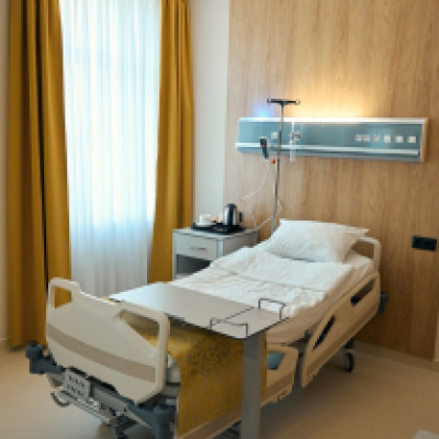 A rehabilitation center room with a hospital bed in the center. The tray rests over the bed, and the curtains are pulled.