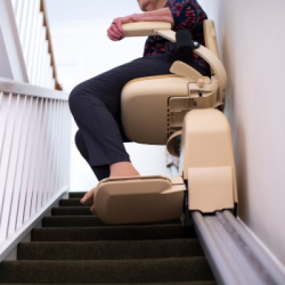 A close-up of a home stairwell with a stairlift user going up the stairs on the lift. The lift is secure to the wall.