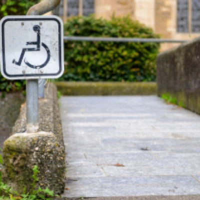 The exterior of a church with a wheelchair accessible sign posted next to the ramp sidewalk. The sidewalk is empty.