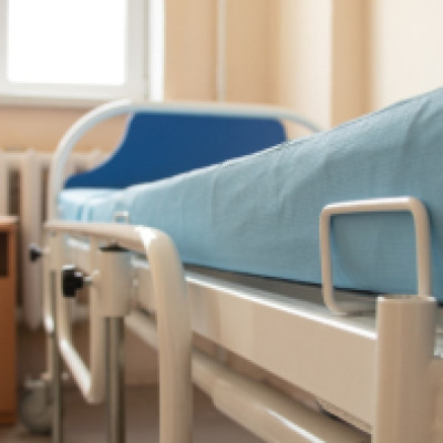 A close-up of the side of a hospital bed with a blue mattress on it. There are no linens and the room is empty.