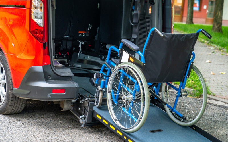 A blue-framed wheelchair sits on the ramp of a vehicle. The vehicle is red and large enough to haul the chair.
