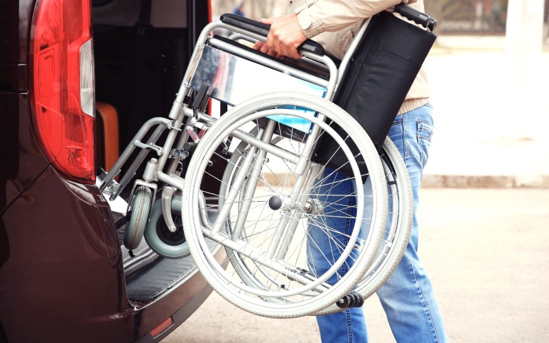 A person loads a wheelchair into the back of their passenger SUV. The wheelchair is folded compactly.