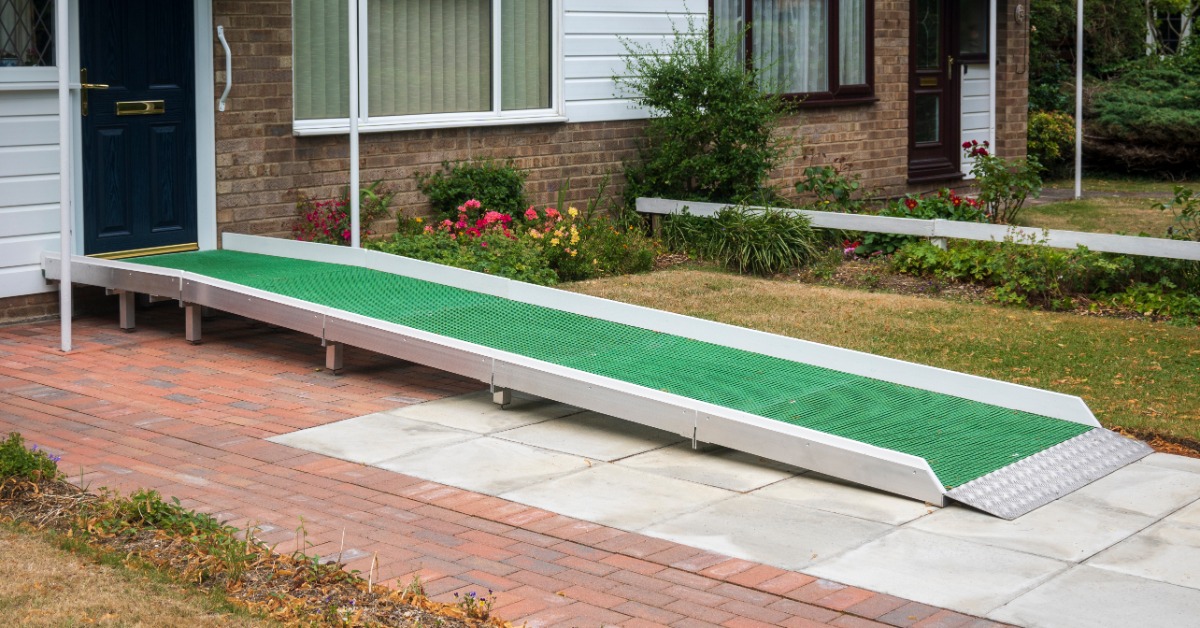 A steel wheelchair ramp located at the front door of a residential property. The ramp has a green carpet.
