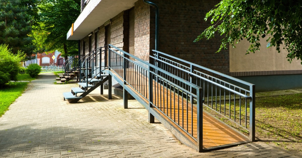 A wheelchair ramp outside a building with a set of small stairs to the left. Both options lead to a doorway.