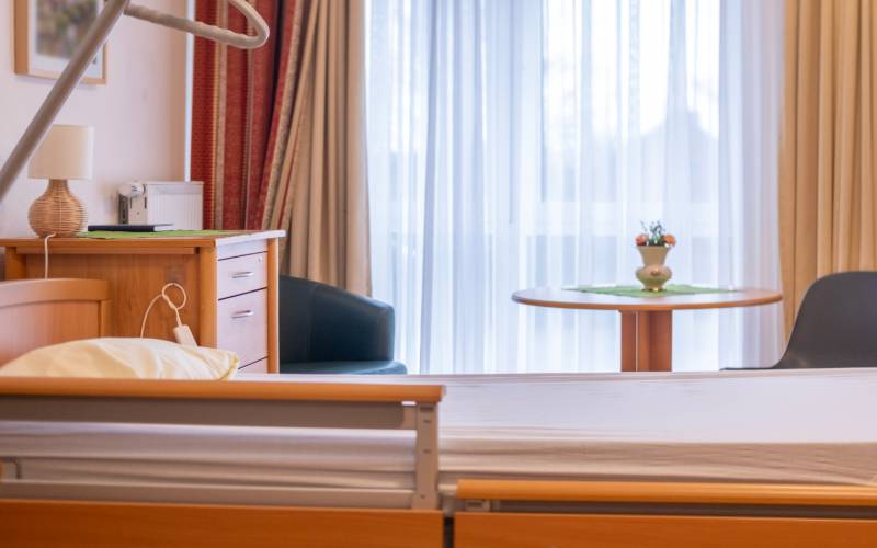 A modern medical facility with home-like features, such as wood tones and a wooden hospital bed. The bed is flat.