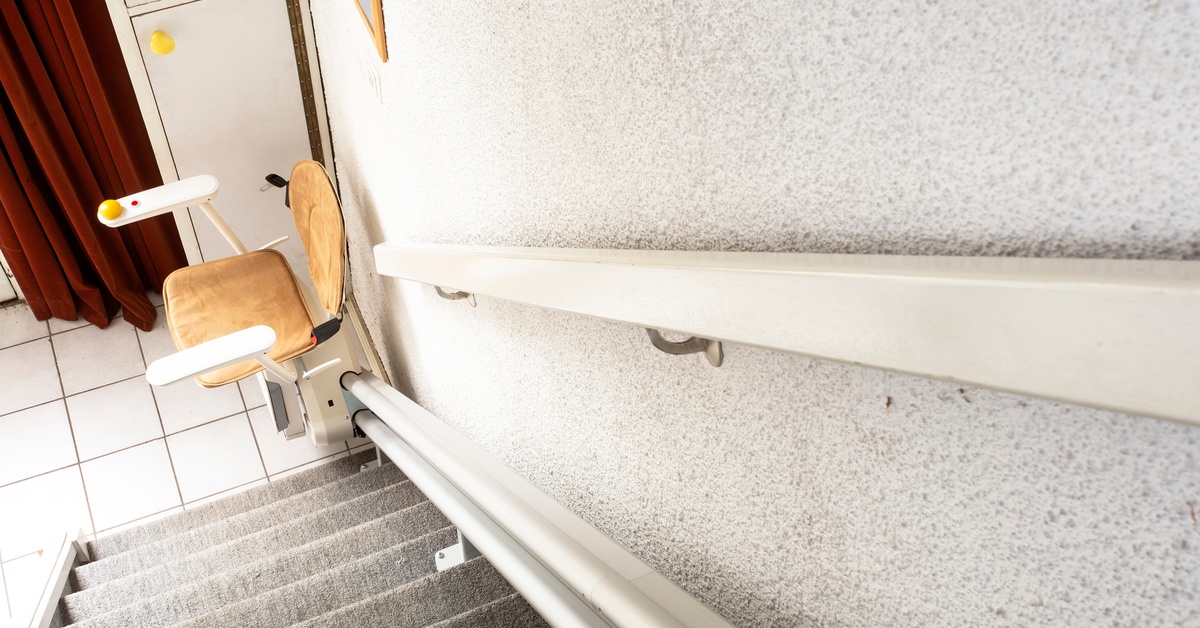 The top of a staircase with a chair at the bottom. The chair attaches to the stairlift along the wall side of the steps.
