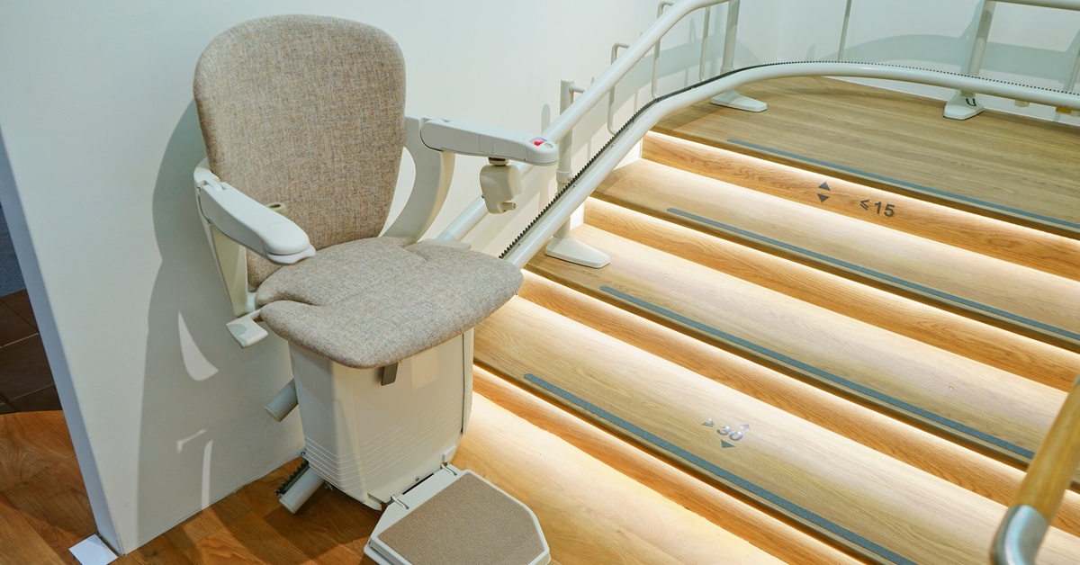 A stairlift chair at the bottom of a curved staircase. The steps have lighting underneath for safety.