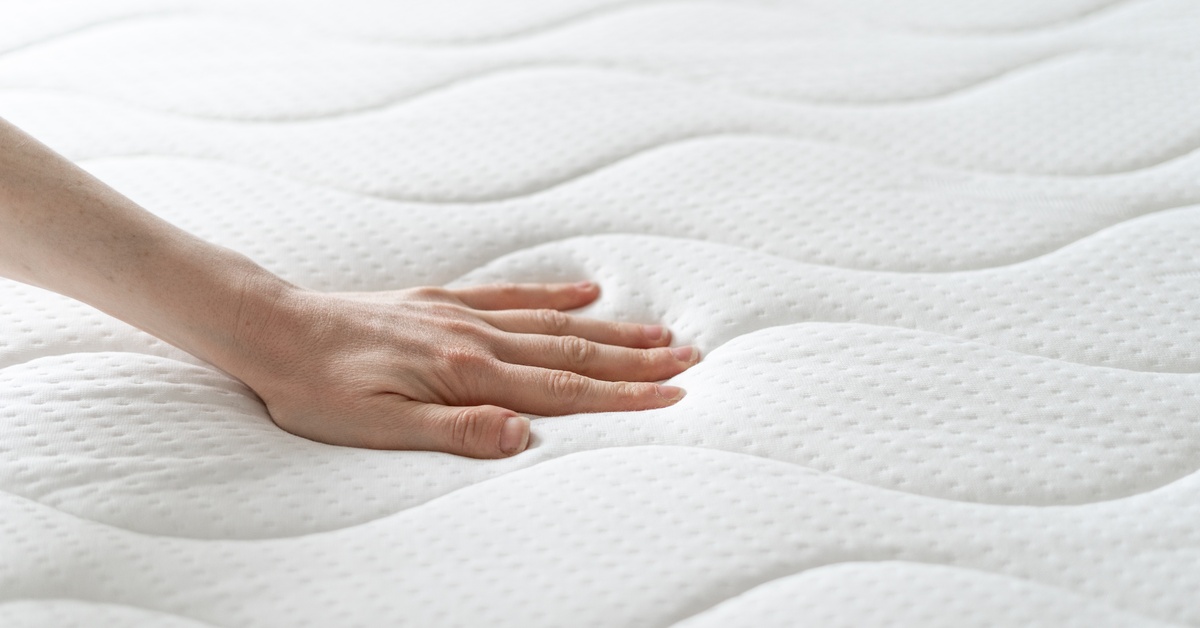 A person pushes on a memory foam mattress designed for a hospital bed. The mattress has curved stitching.