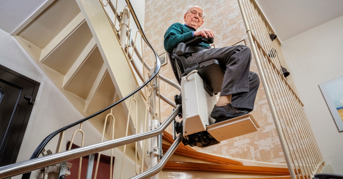 An aging man rides his curved stairlift at home. The stairlift is half-way up the stairwell getting ready to turn.