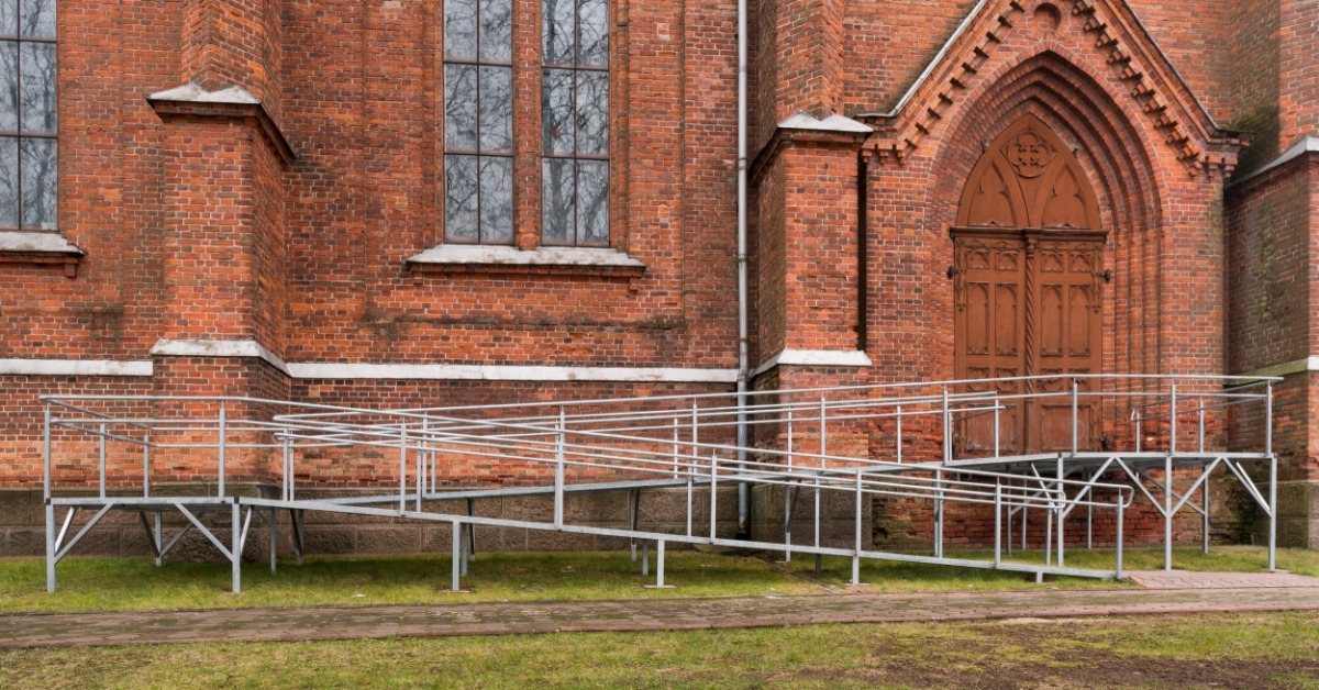 A large red brick church with a metal wheelchair ramp located on the side of the building. The ramp winds around.