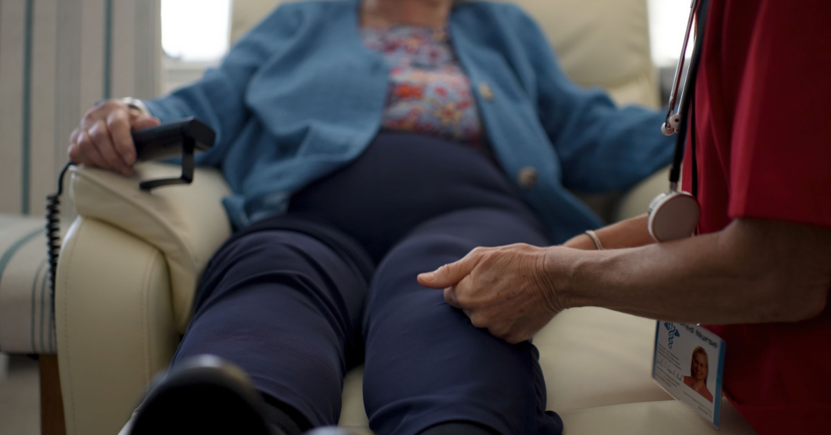 A close-up of a senior patient's legs lifted in their home lift chair. They are holding the remote control in their hand.