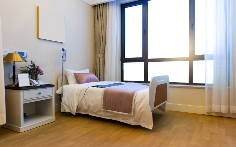A hospital bed made in a rehab facility. There's a nightstand next to the bed with personal items and a lamp.