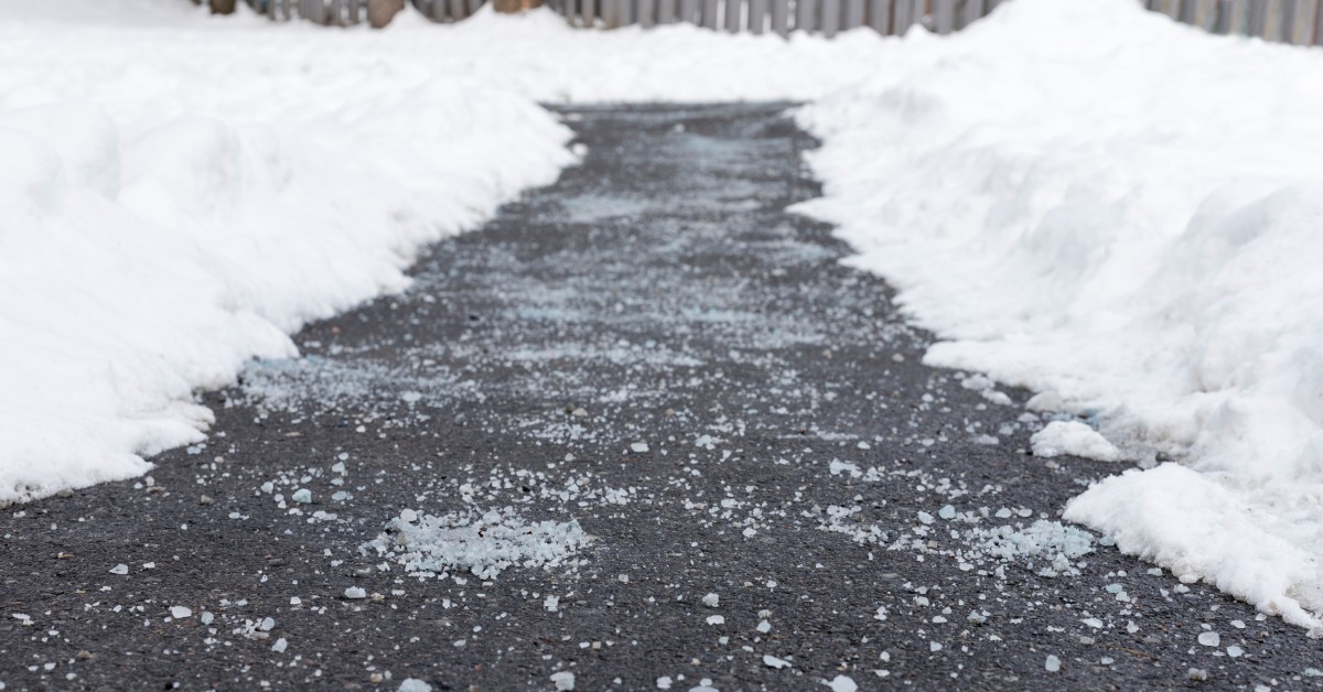 Snow mounds hover a cleared path on the blacktop. The blacktop is clean with rock salt thrown down.