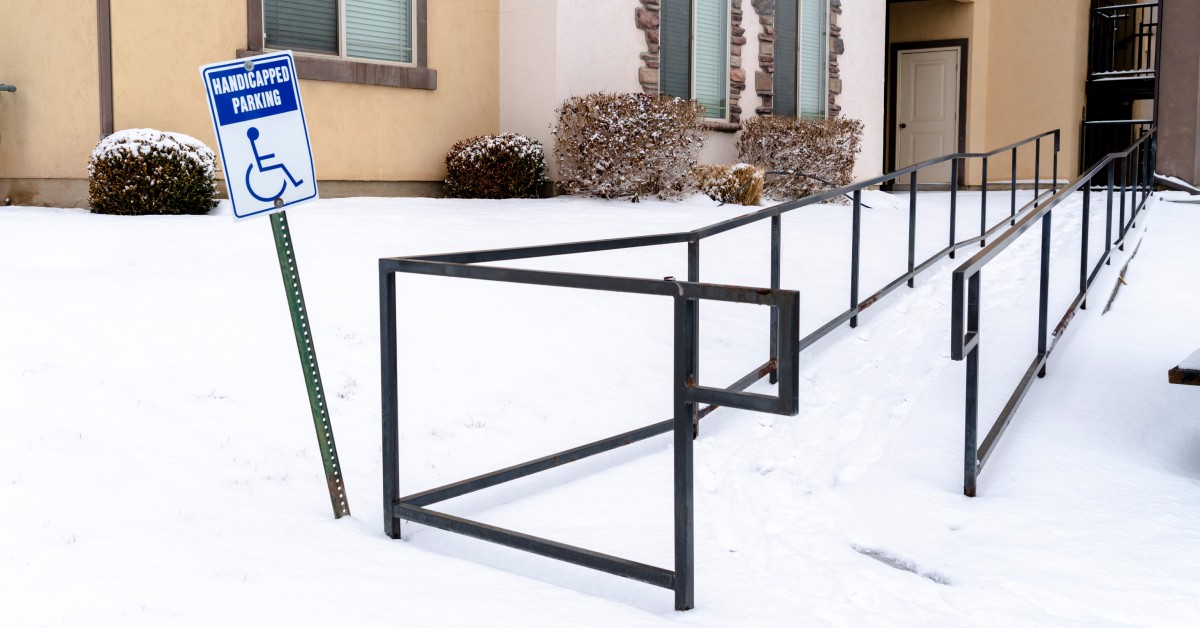 A wheelchair ramp outside of a brick building with a handicap parking sign. The ramp is covered in snow.