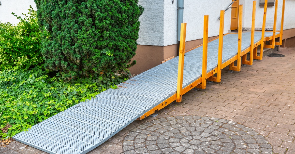 A wheelchair ramp installed on the exterior of a residential building. The ramp is metal with yellow supports.