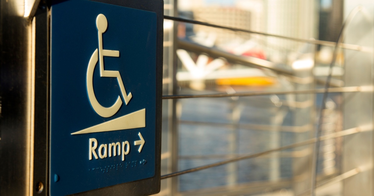 A blue accessibility sign hanging near an entryway. The sign shows a wheelchair user and signals where the ramp is.